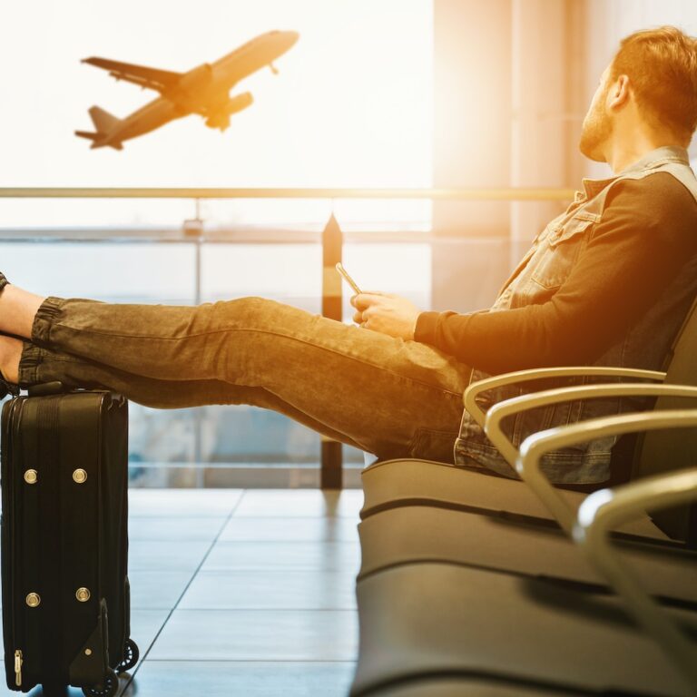 man sitting on gang chair with feet on luggage looking at airplane. Punta Cana Vacation Package